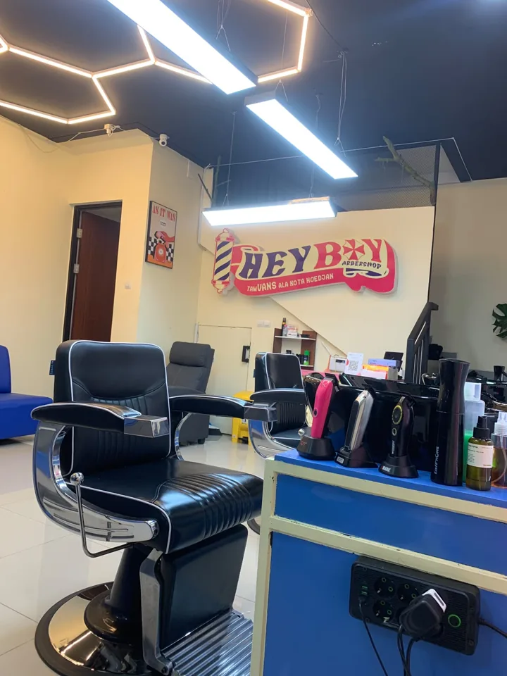 Kursi barber dan area kerja HEYBOY dengan kabinet biru serta logo di dinding