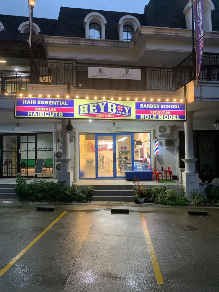 Tampak depan barbershop HEYBOY dengan papan nama menyala saat senja
